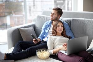 年轻的男人在家里的沙发上看电视，女人在用笔记本电脑＂width=