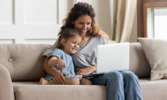 女人和女儿坐在沙发上看着家里的笔记本电脑