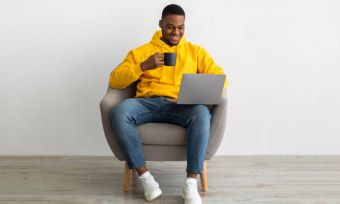 年轻人使用笔记本电脑在黄色的连帽衫,坐在椅子上