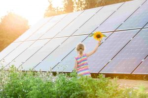 小女孩手里拿着向日葵经过太阳能电池板