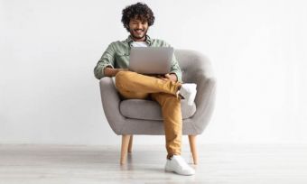 年轻人在灰色连帽衫,坐在椅子上,用一台笔记本电脑