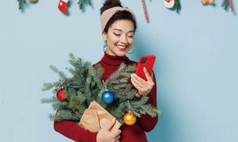 微笑的女人拿着迷你圣诞树和看电话