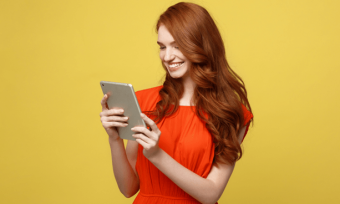 微笑的年轻女孩使用平板电脑与橙色的背景