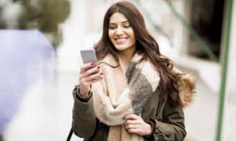 微笑的女人在寒冷的天气中使用智能手机在户外